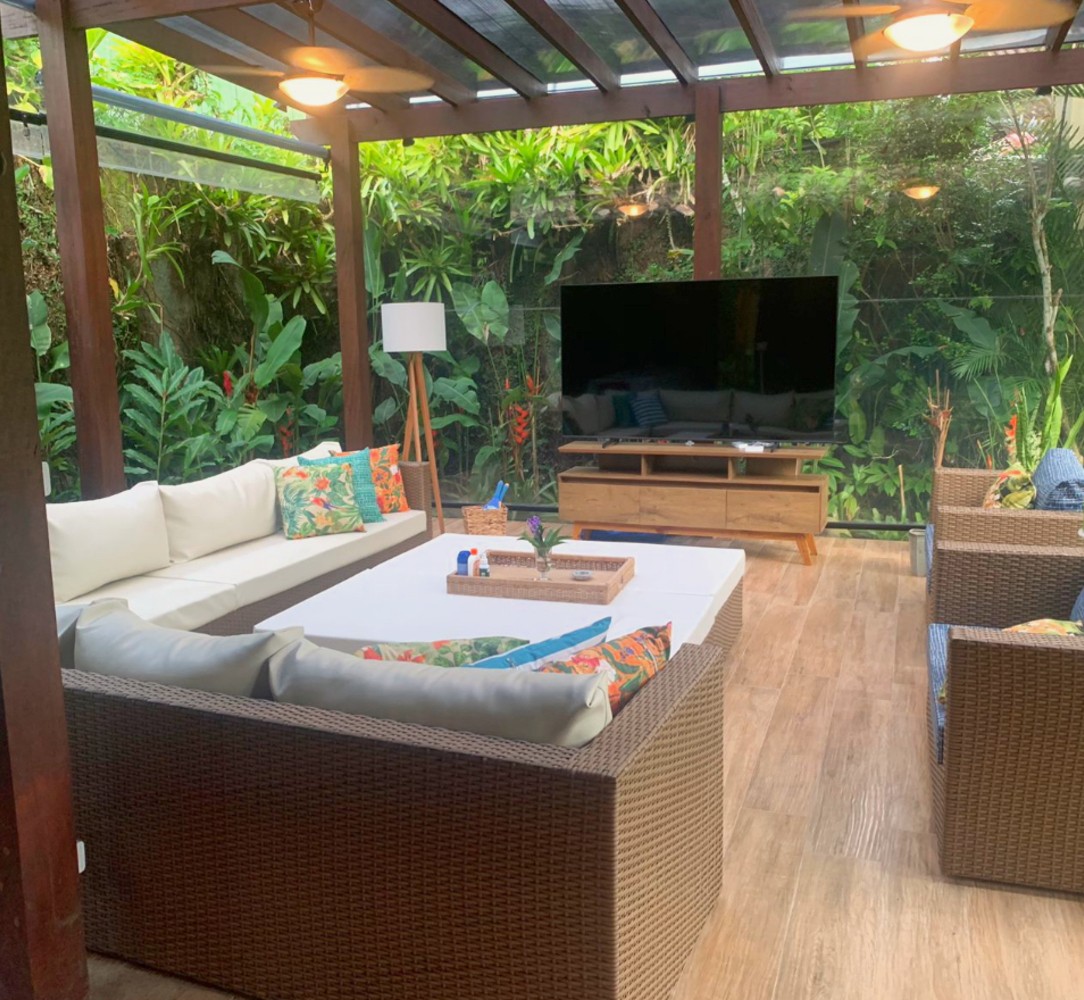 Lounge coberto com sofás, TV e jardim ao fundo